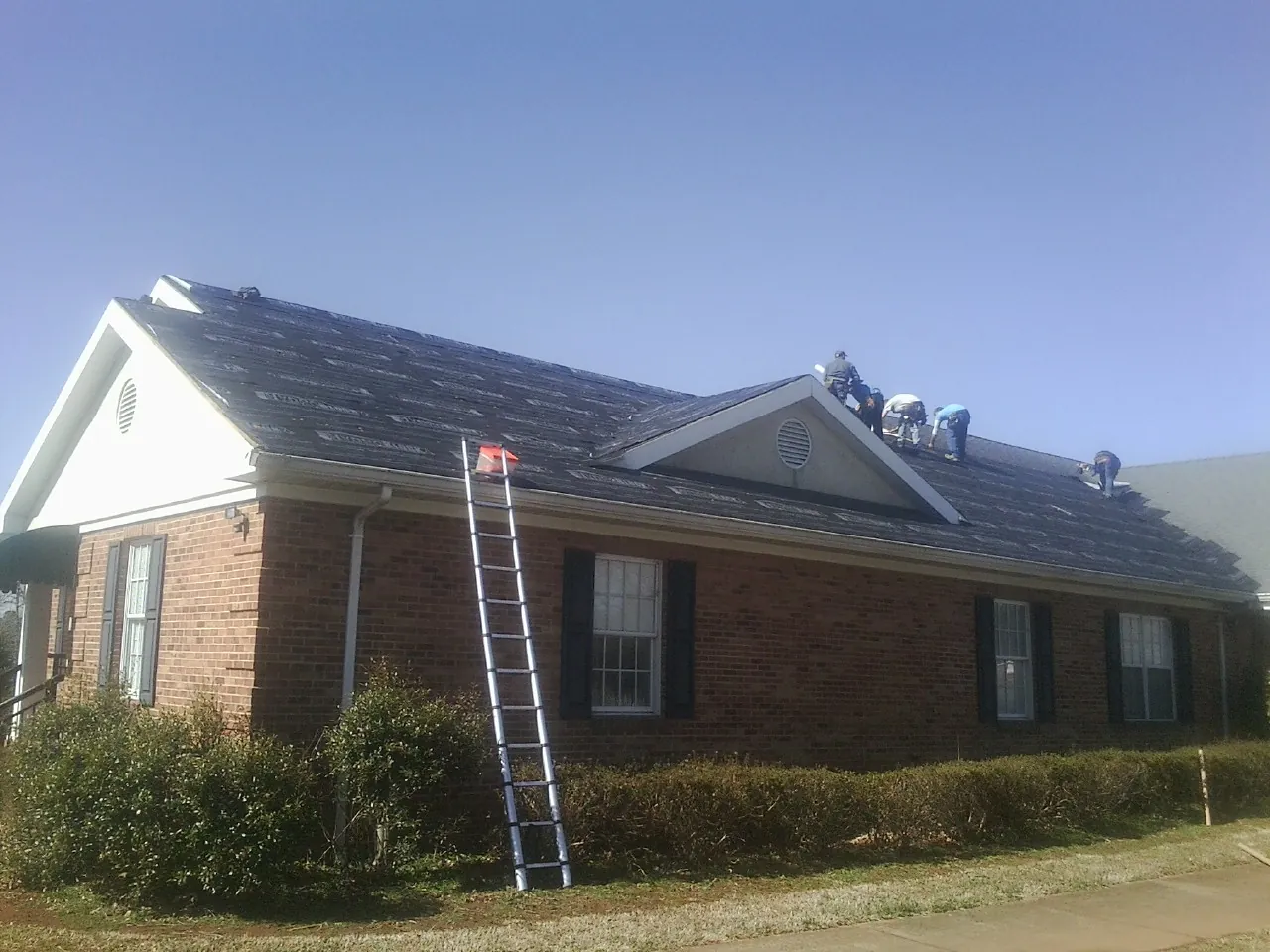 Crew tearing shingles off a brick ranch roof with a ladder set — Emergency Roof Repair work by our crew in Burton