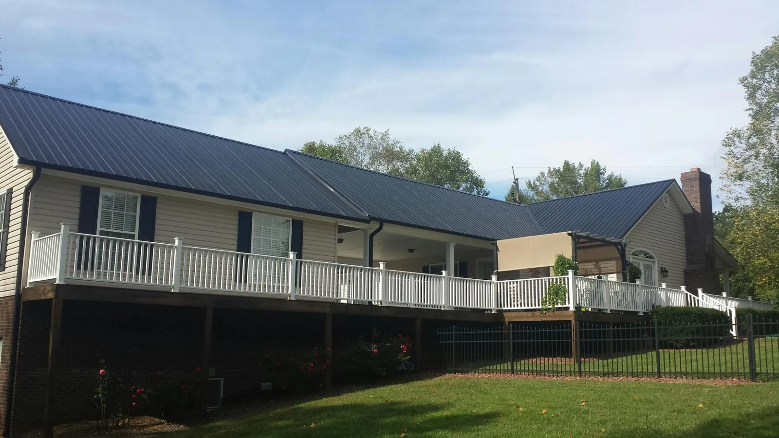 Black metal roof above a long white railed deck on a hillside home in Burton