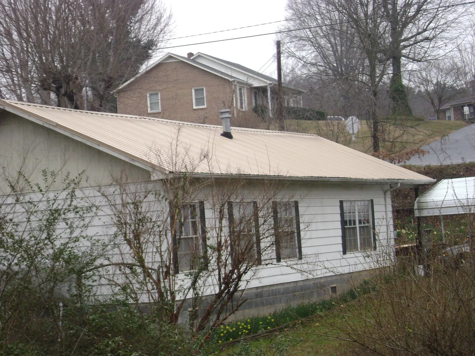 Tan metal roof on a white sided house set into a hillside — Commercial Roofing by Roofing Brothers in Burton